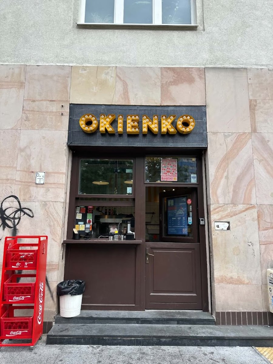 Front OKIENKO z żarówkowym szyldem i czerwonymi skrzynkami Coca-Coli obok