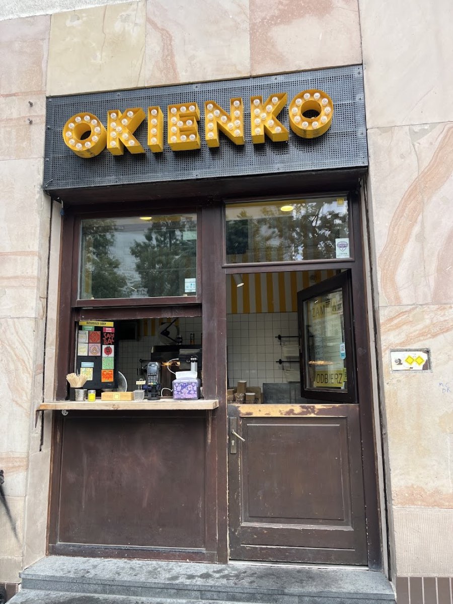 Okienko OKIENKO na Polnej z podświetlonym żarówkowym szyldem nad brązową witryną